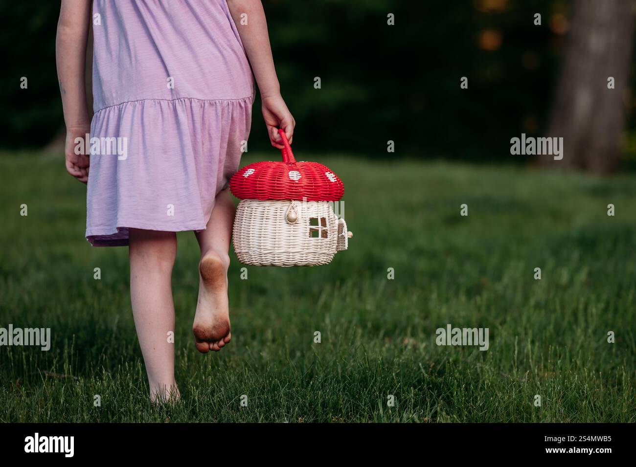 Bambino che cammina a piedi nudi in erba con un cestino a forma di fungo Foto Stock