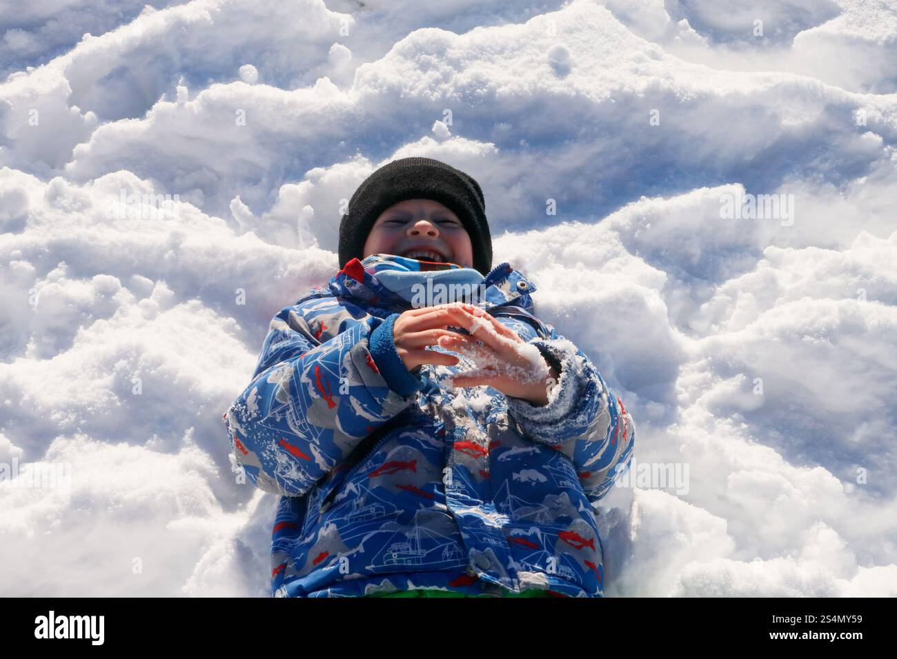 Ragazzo gioioso in giacca e cappello invernali, sdraiato nella neve Foto Stock