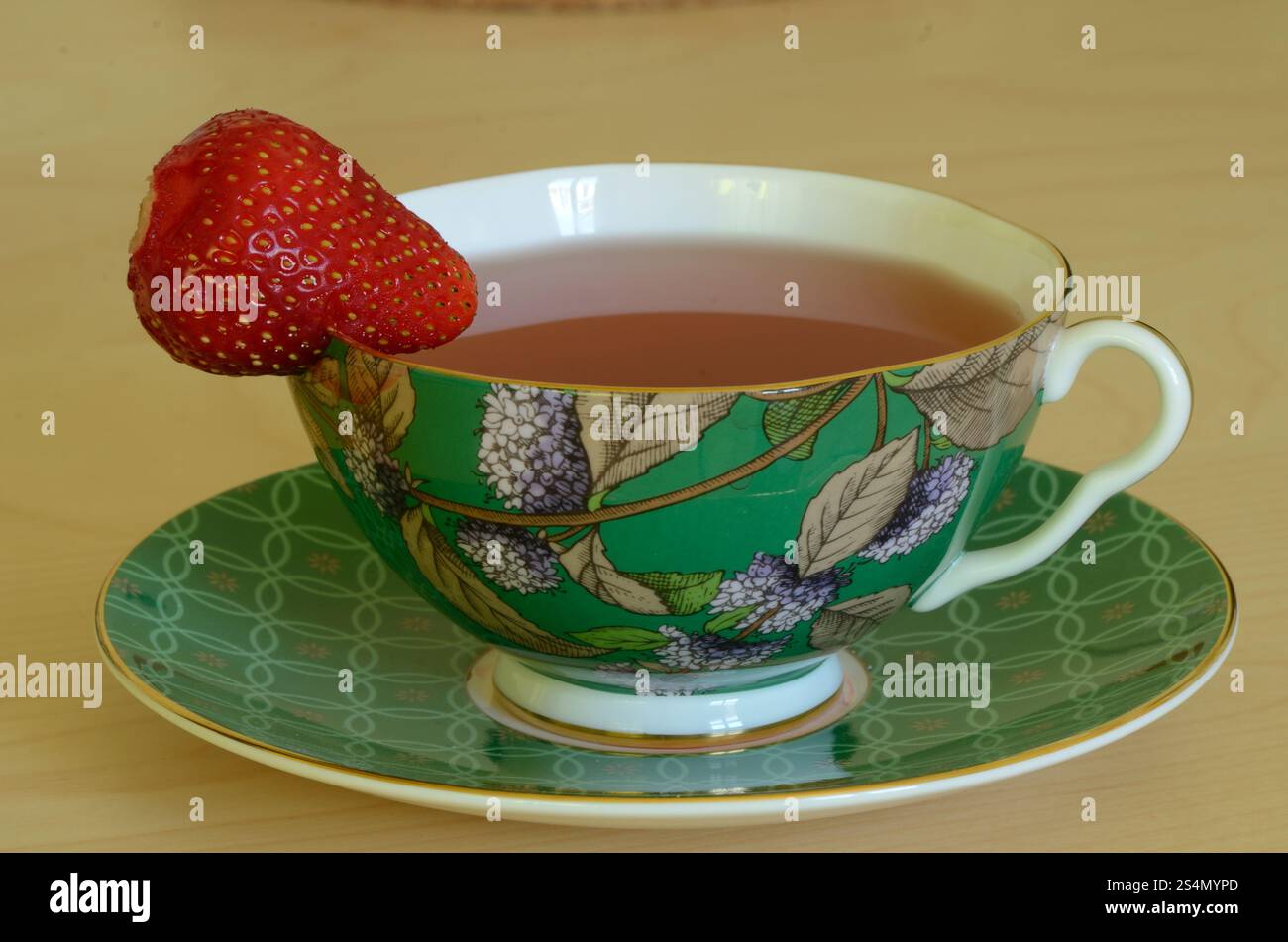 Una bella tazza decorativa riempita di tè e adornata con una bacca Foto Stock