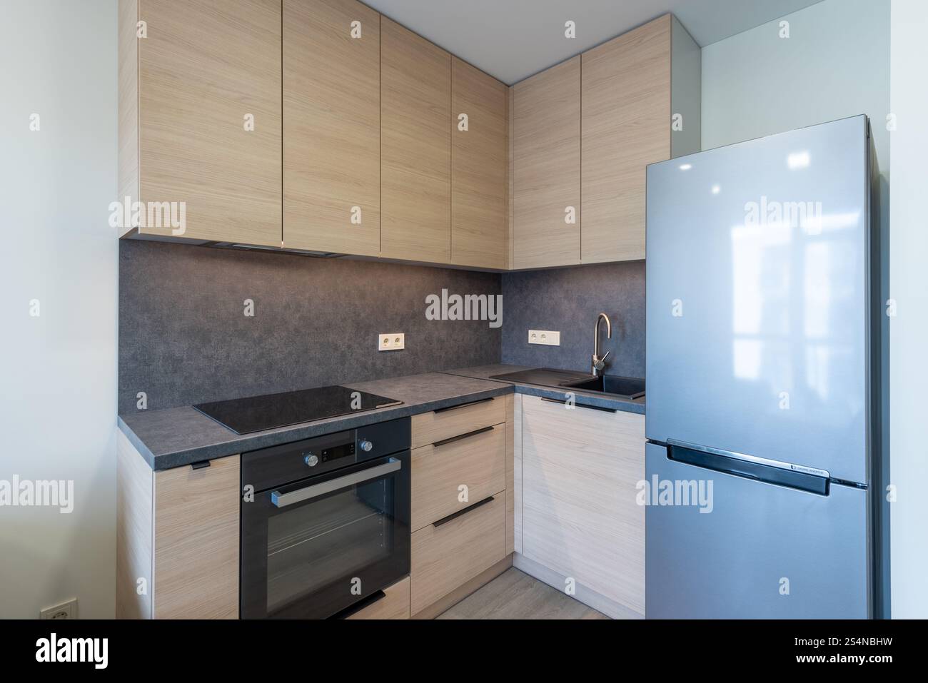 Cucina contemporanea con mobili in legno, forno incorporato, piano cottura elettrico e un elegante frigorifero in acciaio inossidabile. Ideale per abitazioni compatte. Ho Foto Stock