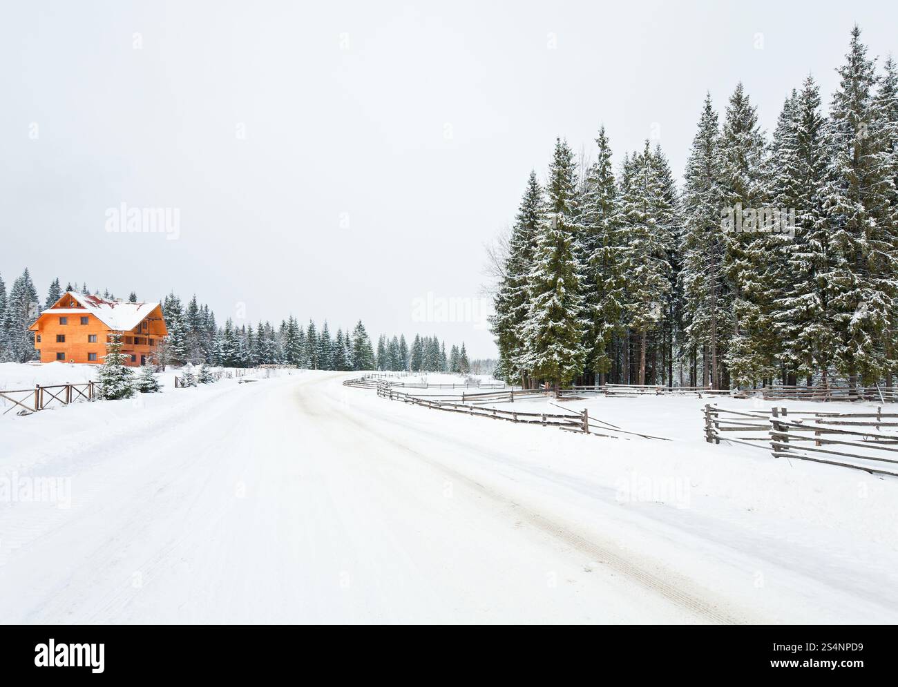 paesaggio montuoso invernale con recinzione, casa in legno e strada di campagna Foto Stock