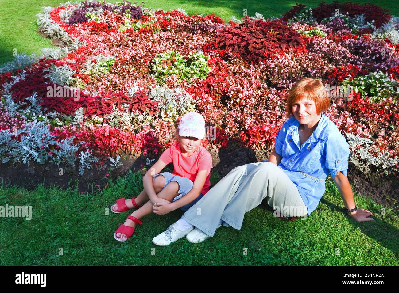 Madre con figlia che riposa vicino alla fioritura colorata aiuola nel parco estivo della città Foto Stock