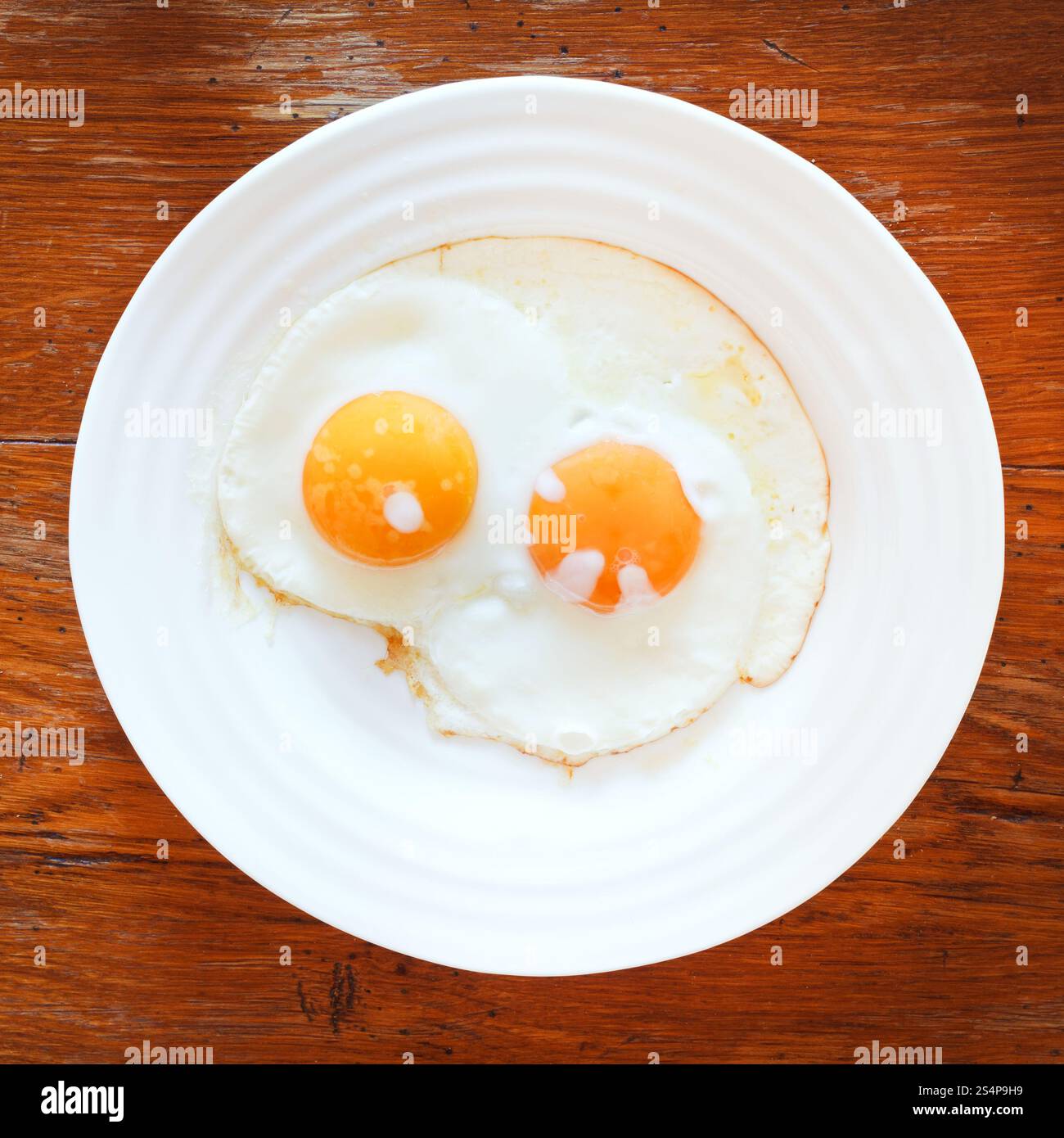 Piastra di colore bianco con due uova fritte sul tavolo di legno Foto Stock