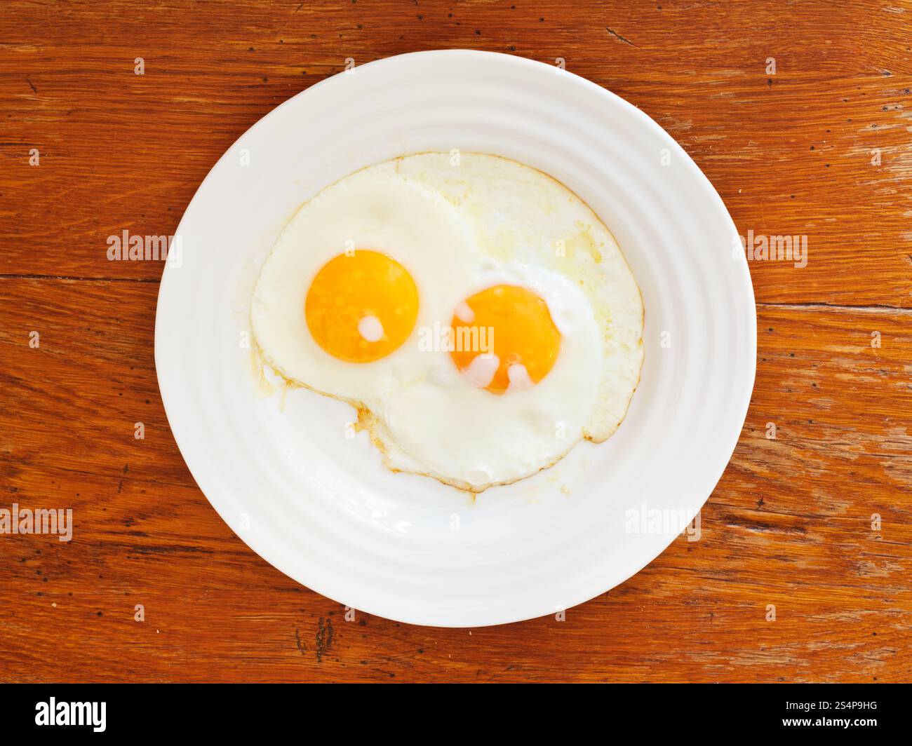 Vista superiore della piastra bianca con due uova fritte sul tavolo di legno Foto Stock