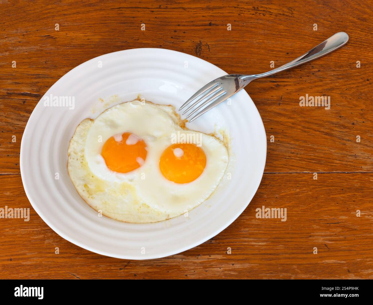 La prima colazione con due uova fritte su piastra bianca sul tavolo di legno Foto Stock