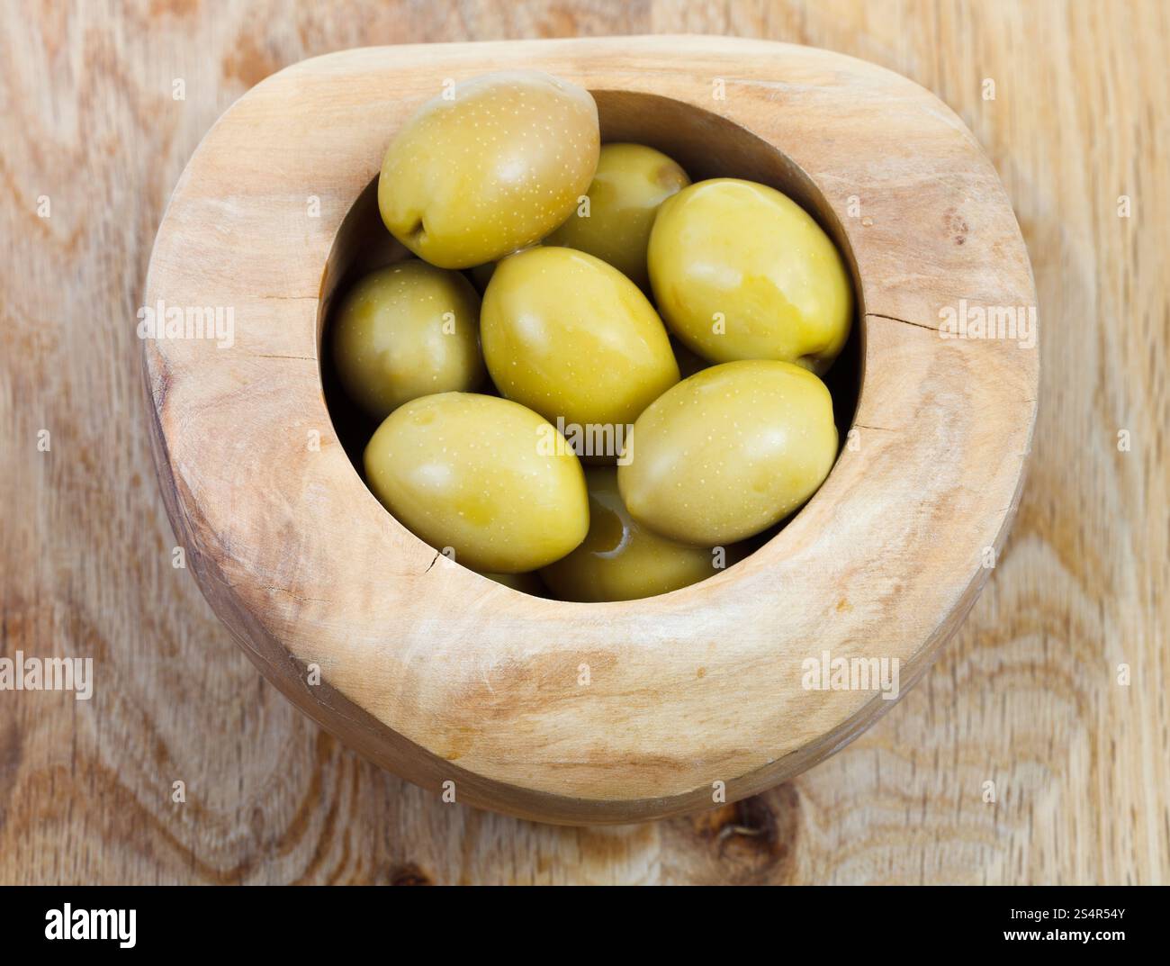 Vista dall'alto di olive verdi in ciotola di legno su piastra in legno Foto Stock