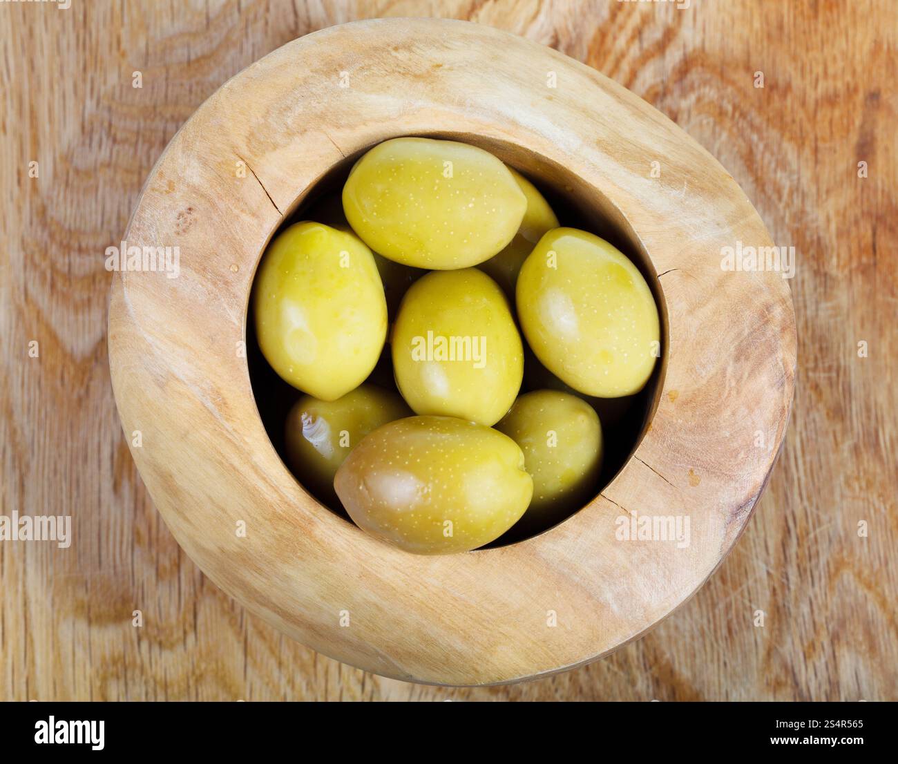 Al di sopra di vista di olive verdi in ciotola di legno su piastra in legno Foto Stock