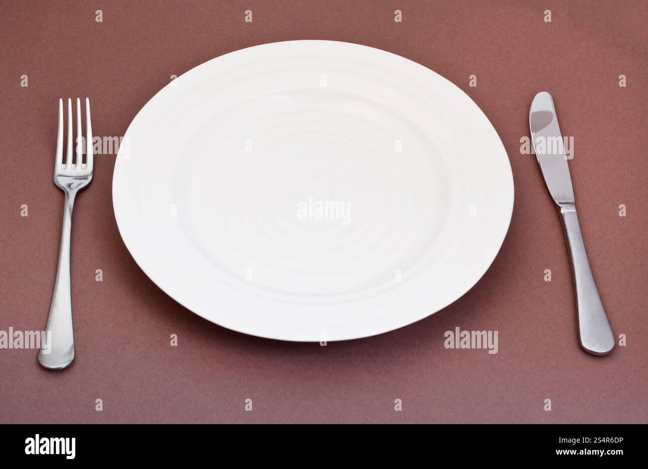 Vuoto piastra bianca con coltello e forchetta impostato su sfondo marrone Foto Stock
