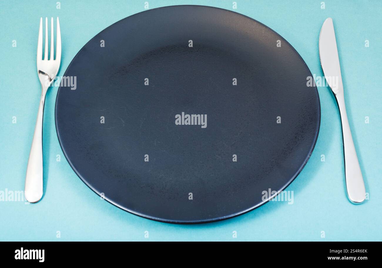 Svuotare la piastra nera con coltello e forchetta impostato su sfondo verde Foto Stock