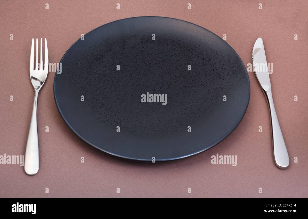 Svuotare la piastra nera con coltello e forchetta impostato su sfondo marrone Foto Stock