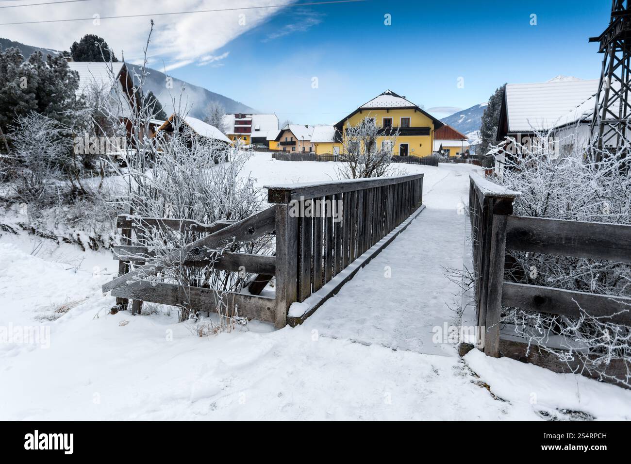 Vecchio piccolo ponte in legno sul fiume di montagna nelle Alpi innevate al giorno Foto Stock