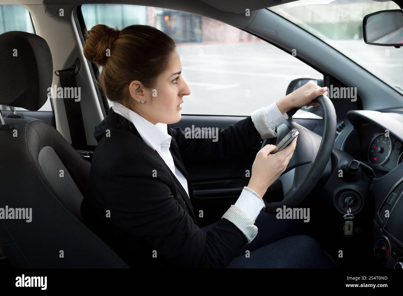 Giovane imprenditrice la digitazione di messaggi mentre si è alla guida di un veicolo Foto Stock