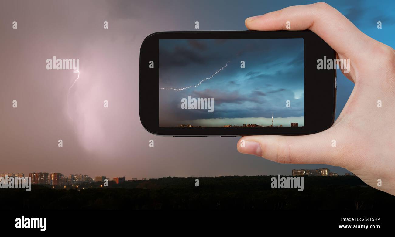 Concetto di viaggio - il turista scatta foto di un fulmine tra le nuvole d'tempesta sulla città in estate su smartphone, Mosca, Russia Foto Stock