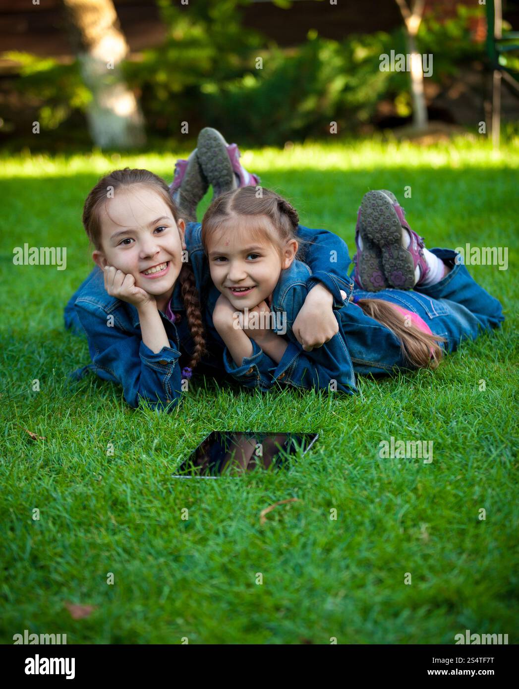 Ritratto di due ragazze che si divertono sull'erba con tablet Foto Stock