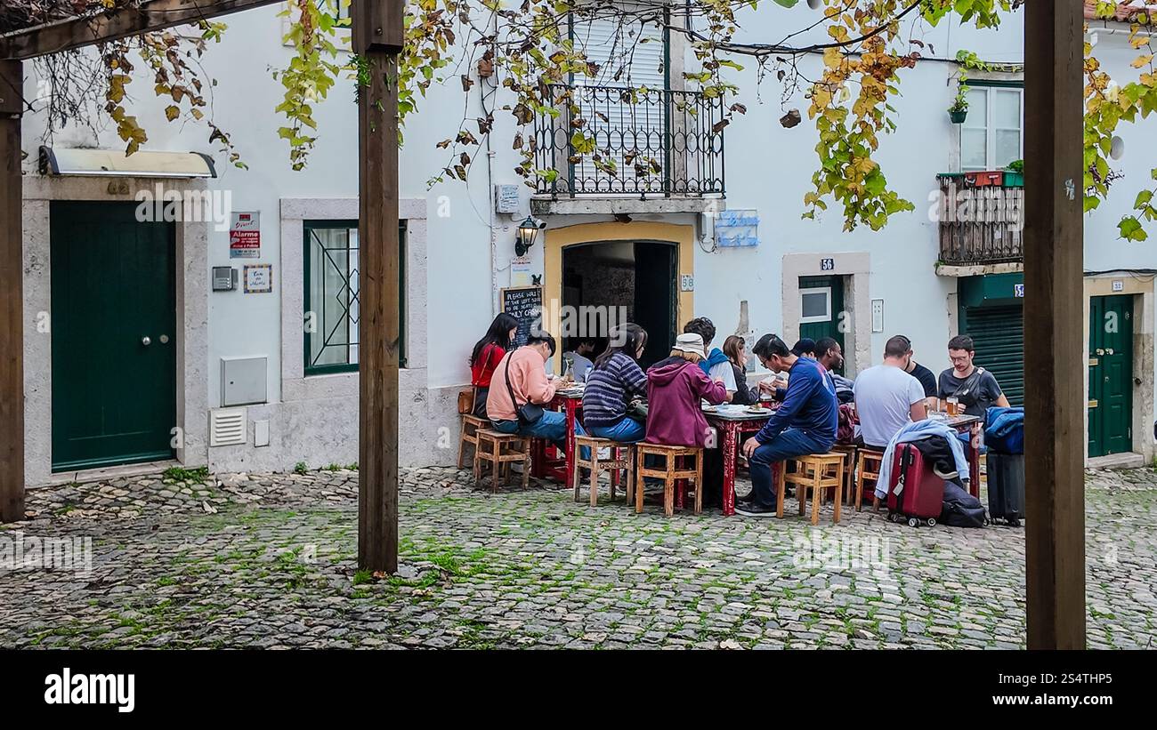 I turisti possono gustare un pasto all'aperto in una caffetteria di Lisbona, in zona Alfama. Foto Stock