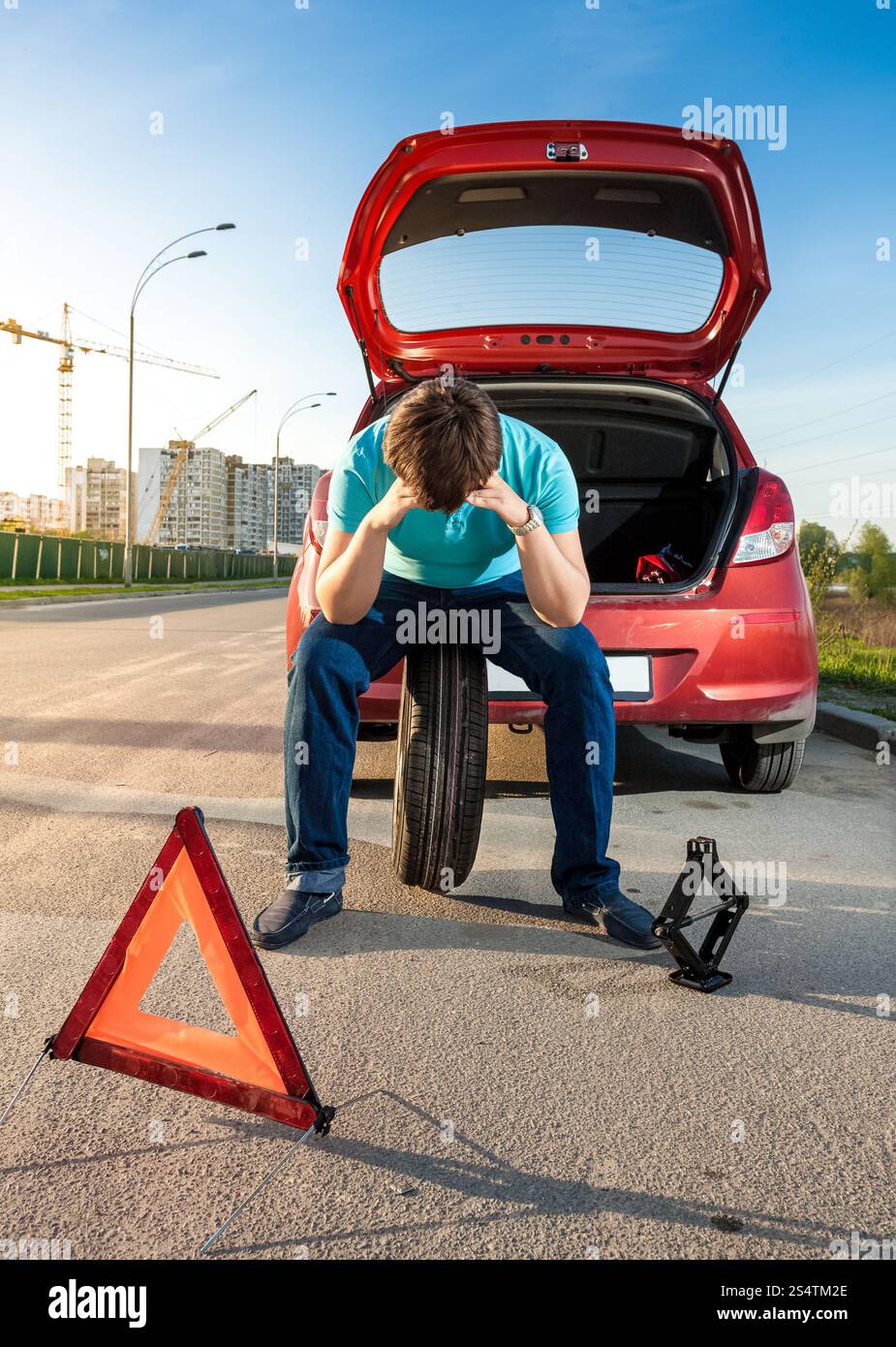 Ritratto di triste uomo seduto sulla ruota di scorta vicino a Broken auto Foto Stock