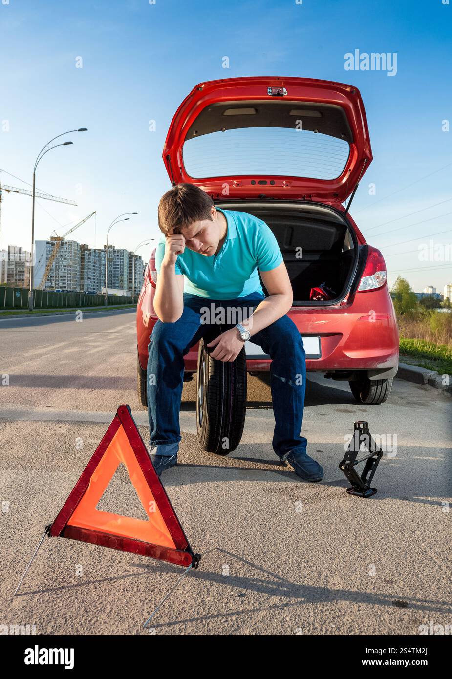 Premuto uomo seduto sulla ruota di scorta vicino a Broken auto Foto Stock