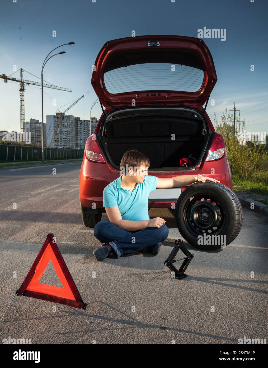 Giovane uomo seduto sulla strada e appoggiata contro broken auto Foto Stock