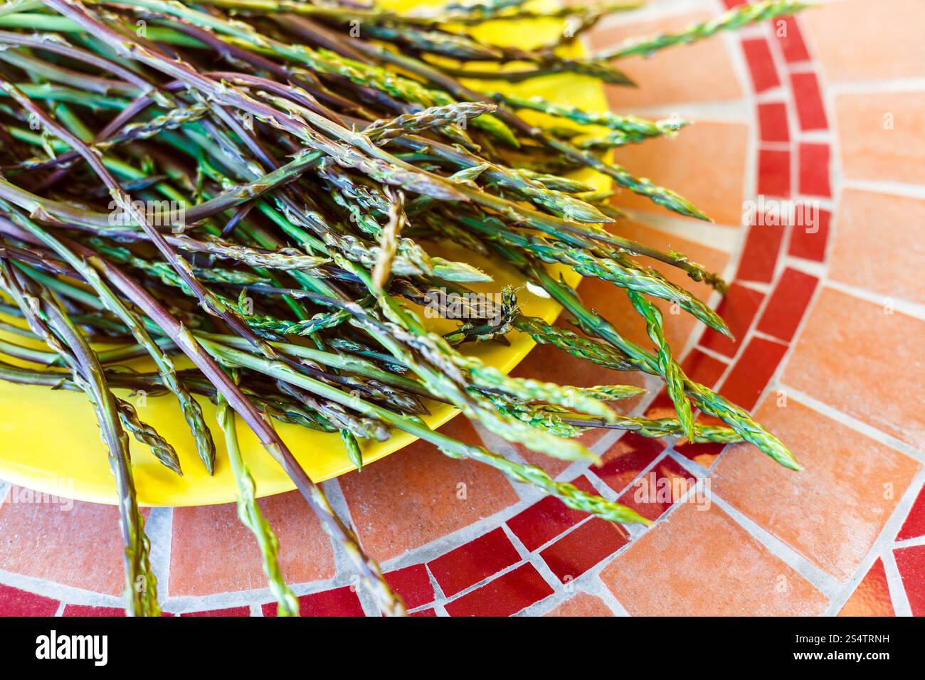 Asparagi verdi selvatici germogli su piastra di colore giallo Foto Stock