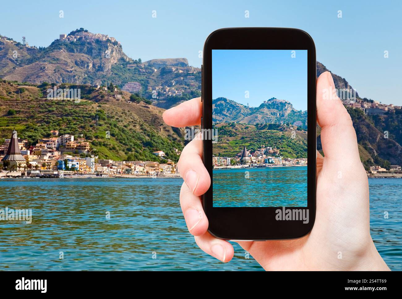 Concetto di viaggio - il turista scatta foto di Taormina, popolare località turistica in montagna e della spiaggia di Gardini Naxos, Sicilia, su smartphone Foto Stock