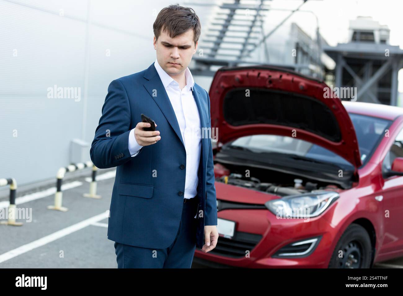 Giovane imprenditore permanente al broken auto e utilizzando il telefono Foto Stock