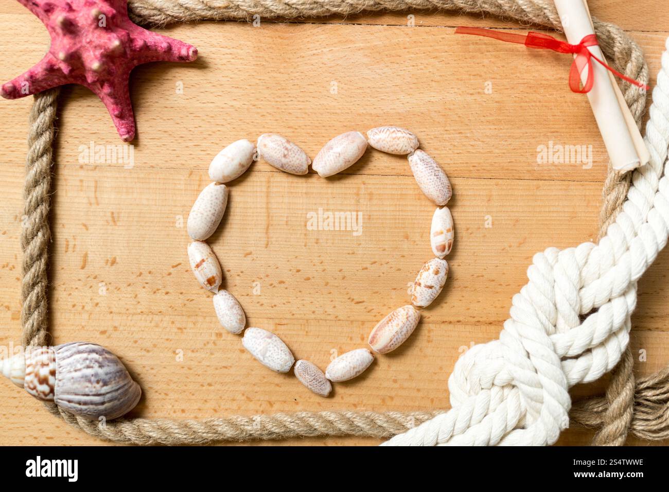 Cuore fatta di conchiglie con bordo di corde e nodi su sfondo di legno Foto Stock