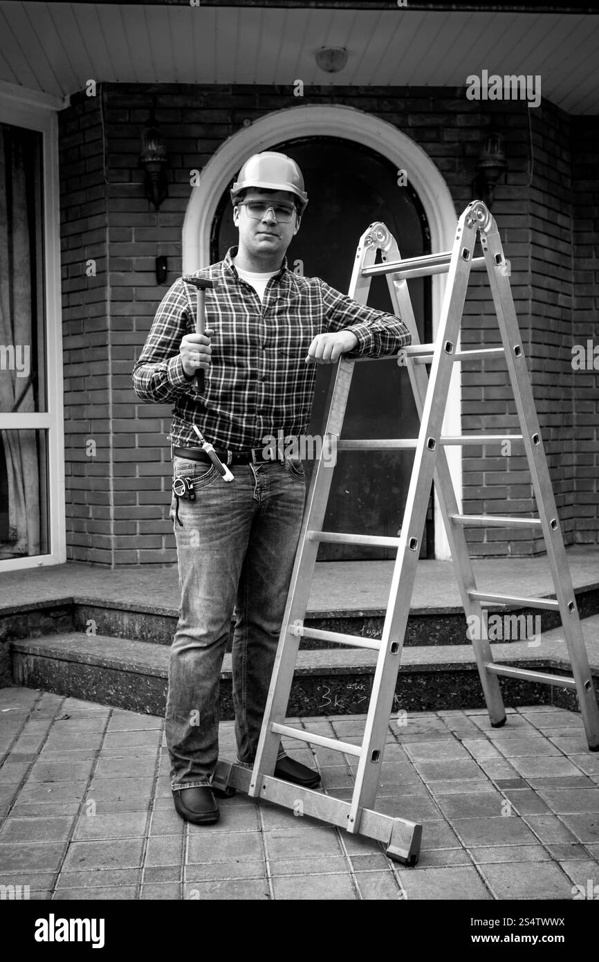 Bianco e nero colpo di lavoratore sorridente in posa con strumenti a scala di metallo Foto Stock