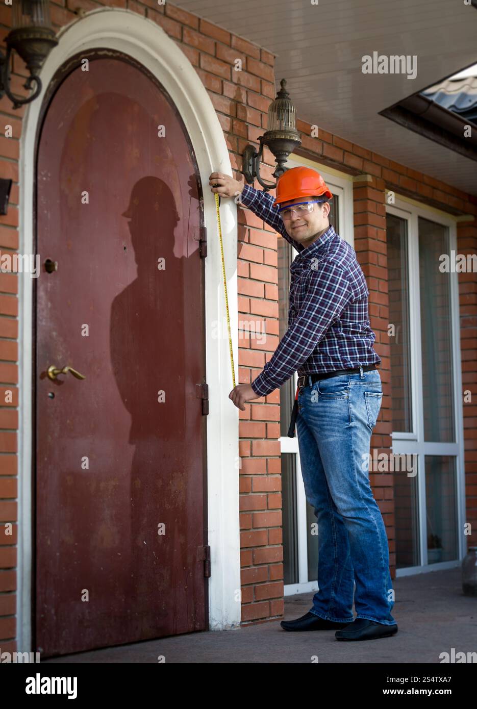 Giovane lavoratore professionale misurando la porta di metallo con nastro Foto Stock