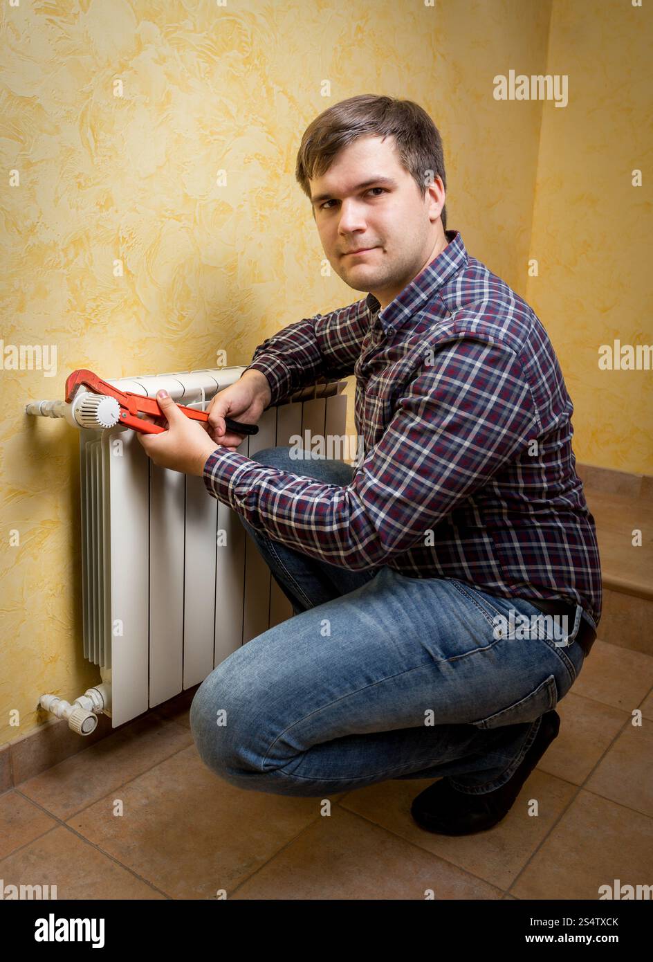 Sorridente giovane pinze di trattenimento e installazione valvola del radiatore Foto Stock