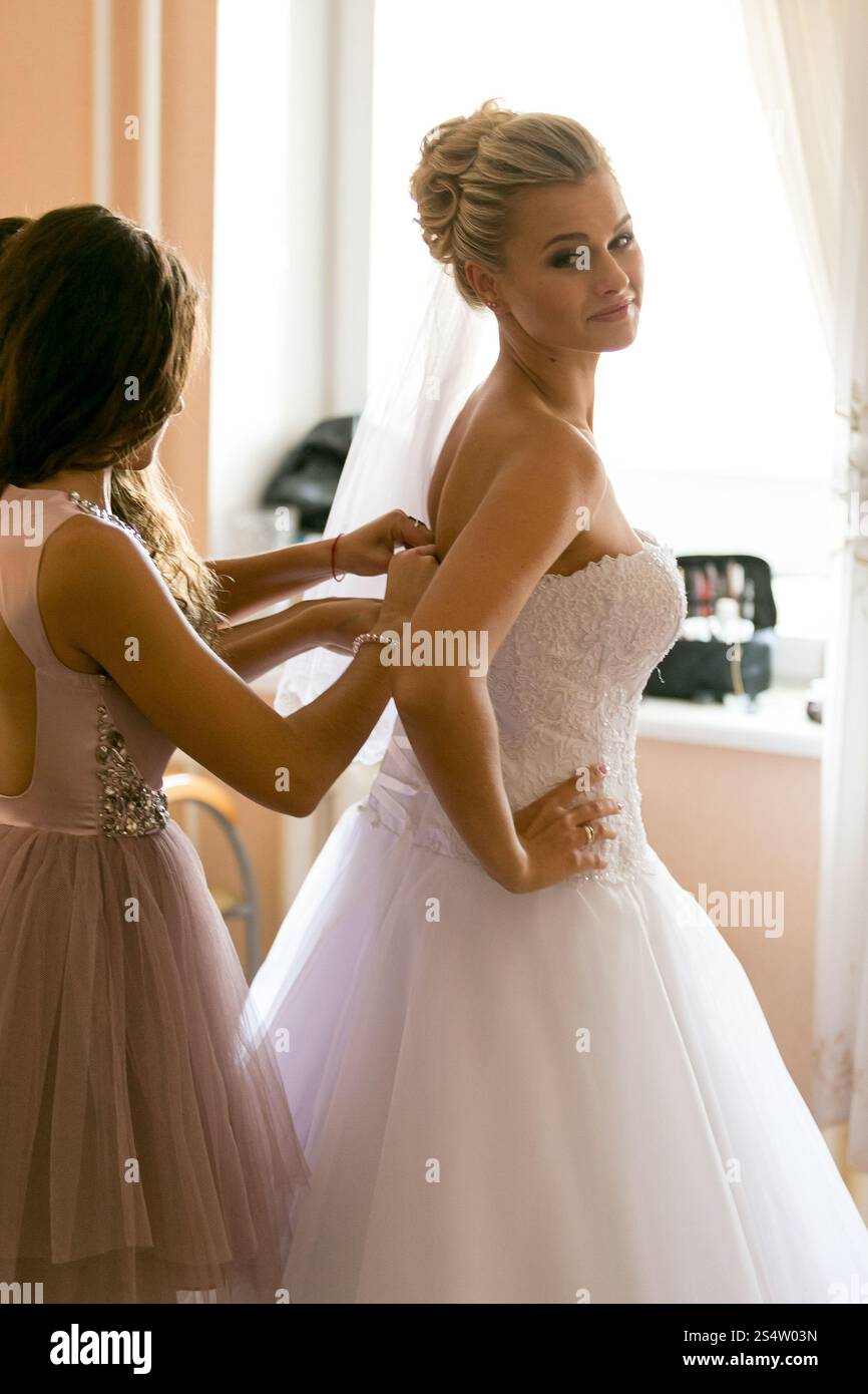 Ritratto di madre che assiste la sposa a indossare l'abito da sposa Foto Stock