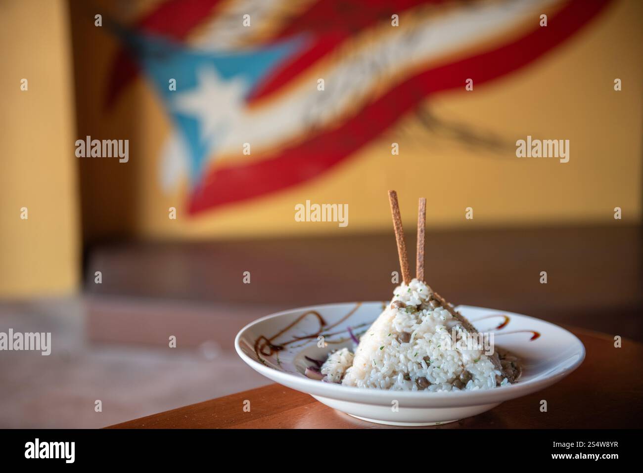 Arroz con Gandules portoricano (piselli e riso) modellato ad arte in un piramico su un piatto guarnito con murale della bandiera portoricana sfocato in bac Foto Stock