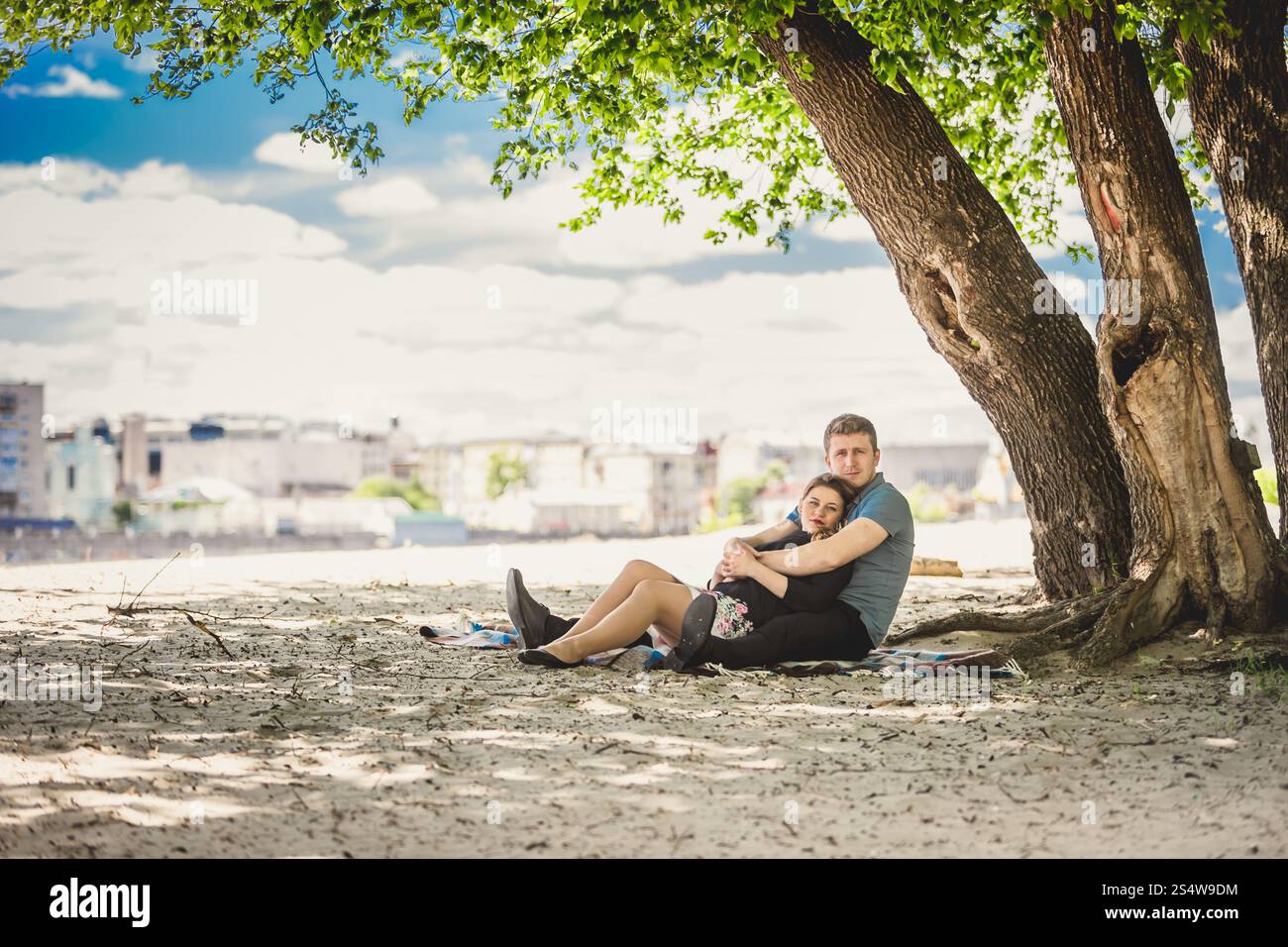 Foto tonificata di una bella coppia innamorata che si rilassa sotto l'albero sulla riva del fiume Foto Stock