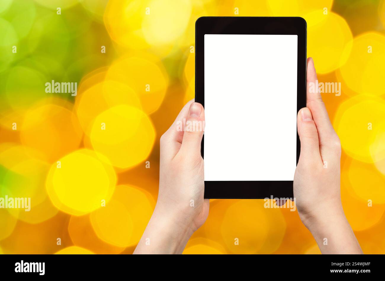 Il concetto della festa di natale è accompagnato da un tablet pc con schermo ritagliato sullo sfondo di grandi luci di Natale gialle e verdi scintillanti Foto Stock