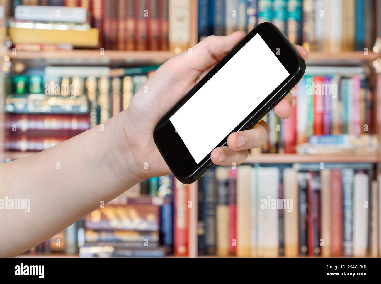 Mano trattiene smart phone con taglio fuori schermo in biblioteca Foto Stock