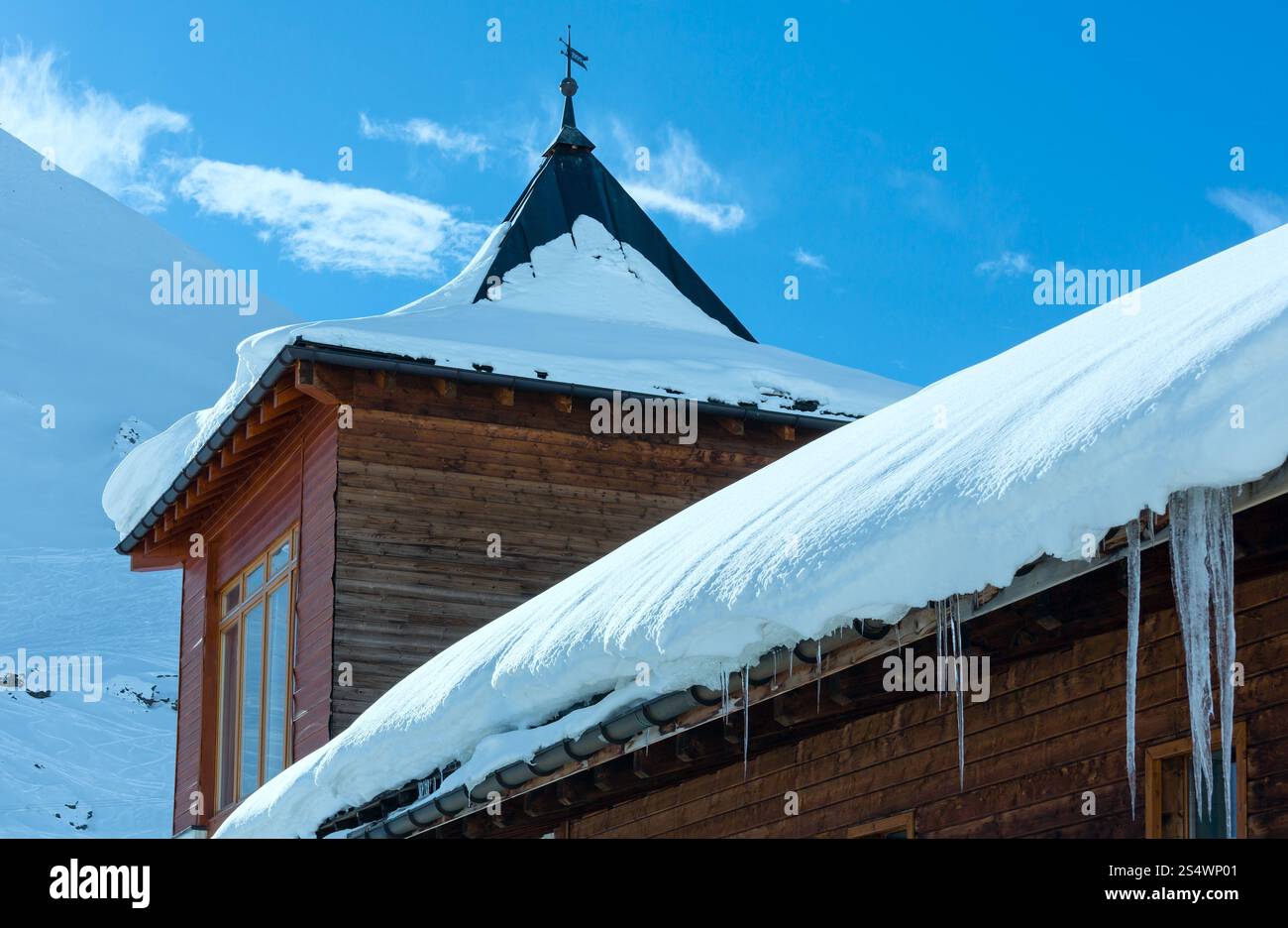 Casa in legno (con neve e ghiaccioli sul tetto) sulla montagna invernale di pendenza. Foto Stock