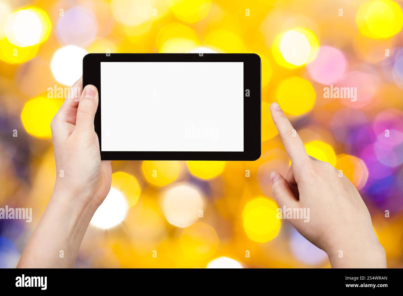 Concetto di festa di natale - mano con tablet pc con schermo ritagliato sullo sfondo da scintillanti luci natalizie gialle e viola bokeh di elettricità Foto Stock