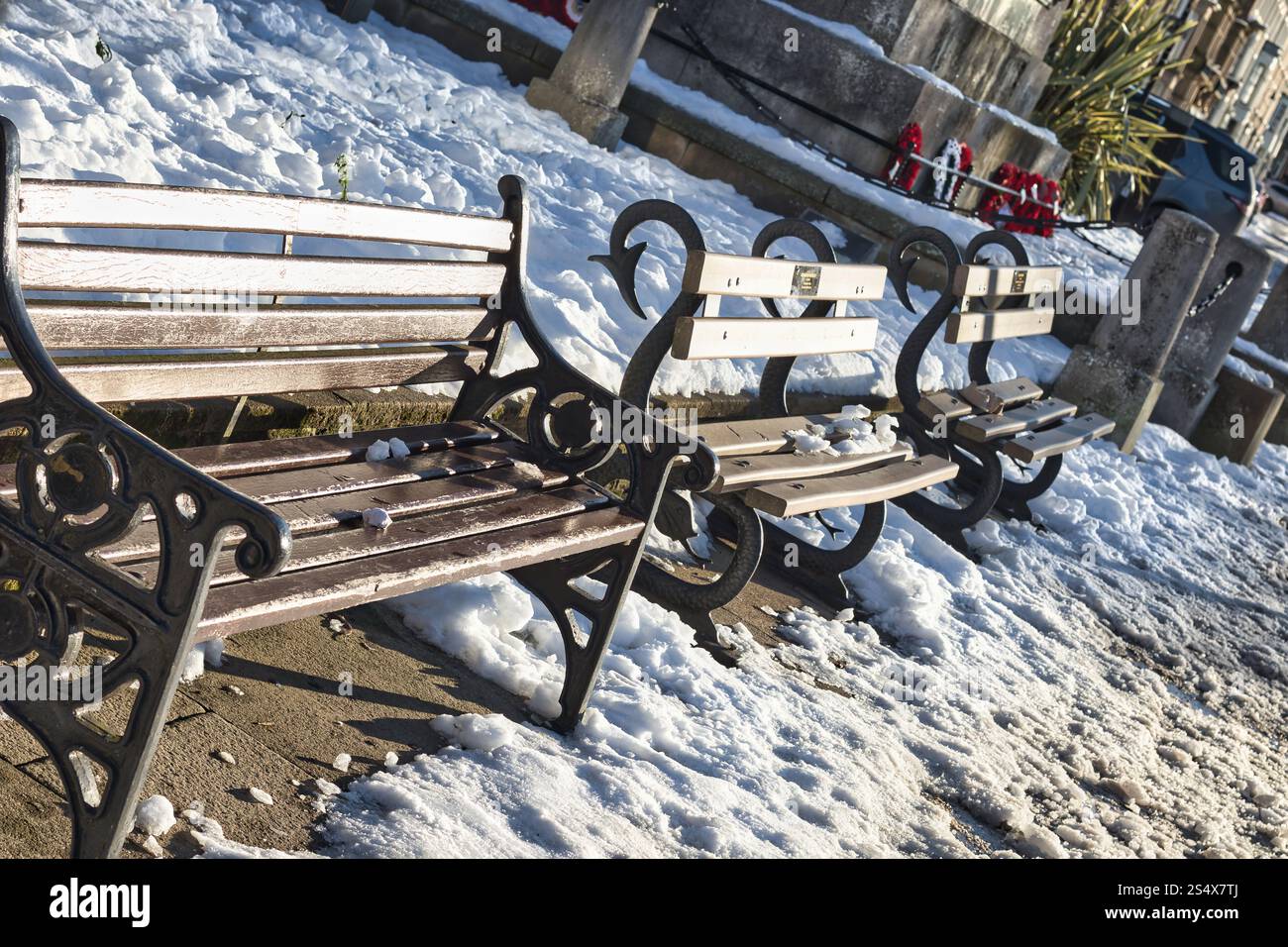 Tre panchine, due in legno di colore chiaro e uno di colore scuro, si trovano su una superficie di cemento innevato. Le panchine hanno ornati in metallo. Neve Foto Stock