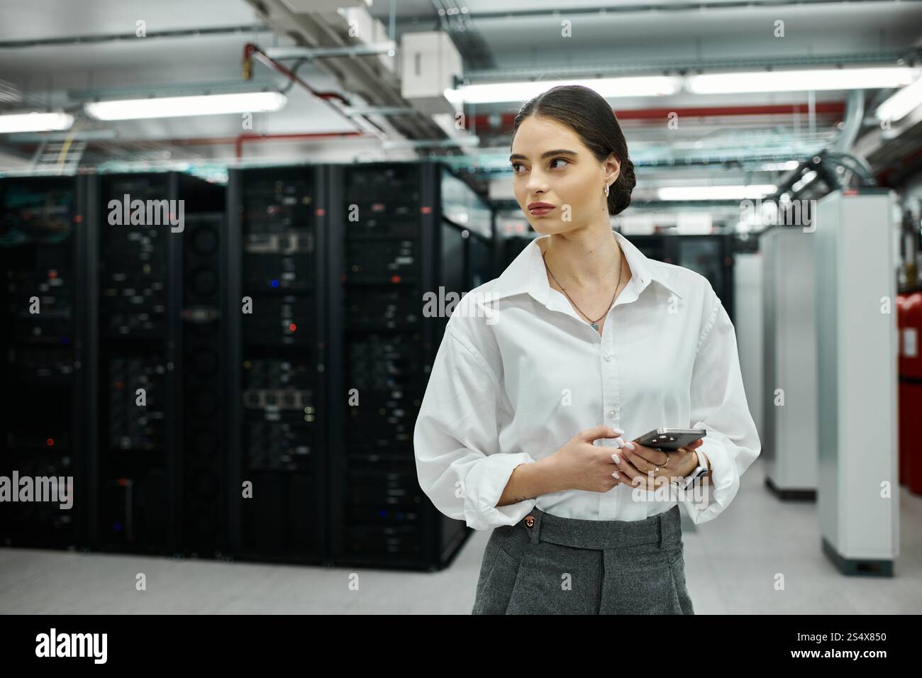 Specialista IT dedicato in una camicia bianca monitora lo stato dei server in un ambiente high-tech. Foto Stock