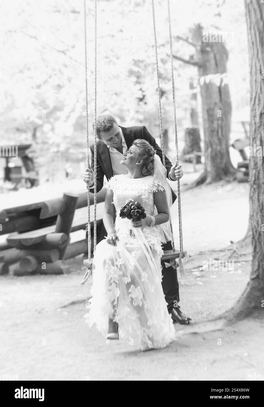 Foto in bianco e nero degli sposi che si baciano felici sull'altalena nella foresta Foto Stock