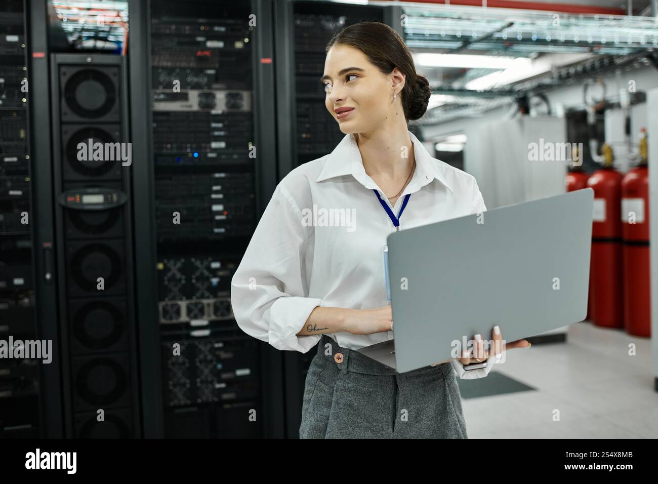 Una donna sicura di sé con una camicia bianca si impegna con il suo notebook in una sala server all'avanguardia. Foto Stock