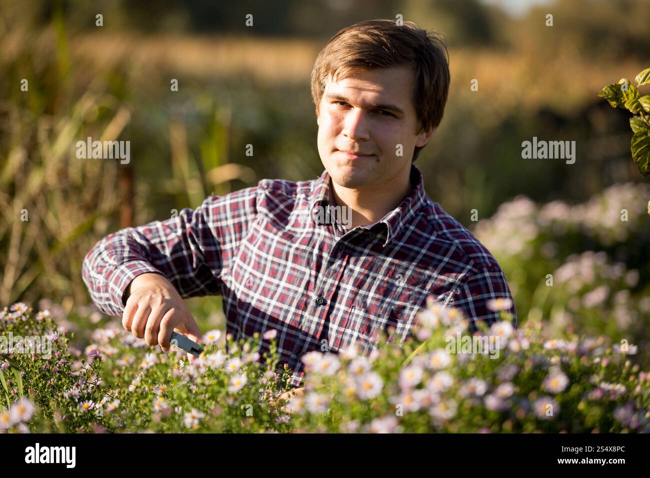 Tonica Ritratto di giovane uomo sorridente la potatura di fiori in giardino Foto Stock