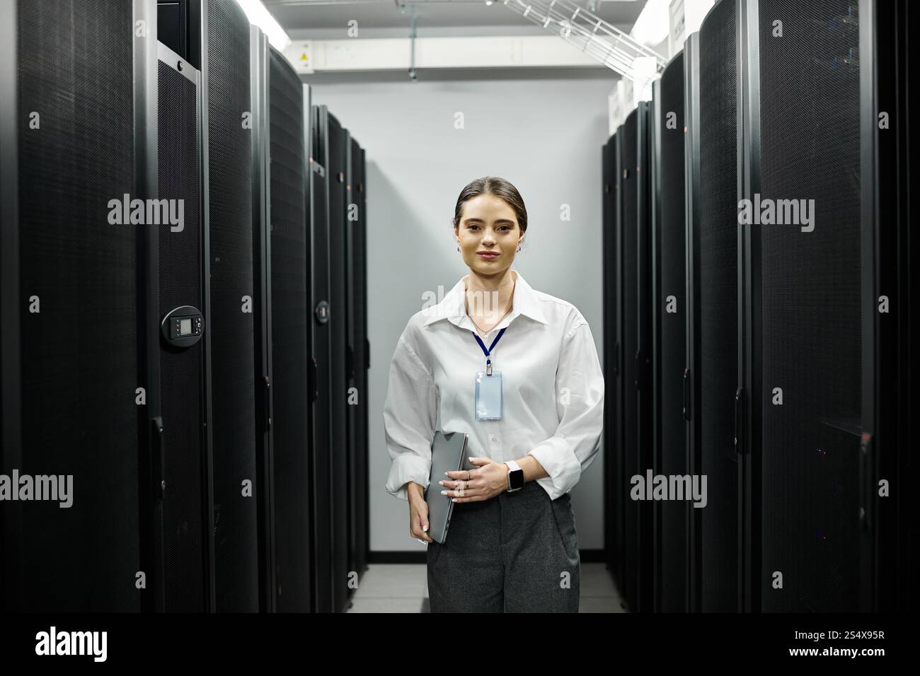 Una donna dedicata con una camicia bianca lavora diligentemente in una sala server high-tech, mantenendo i sistemi. Foto Stock