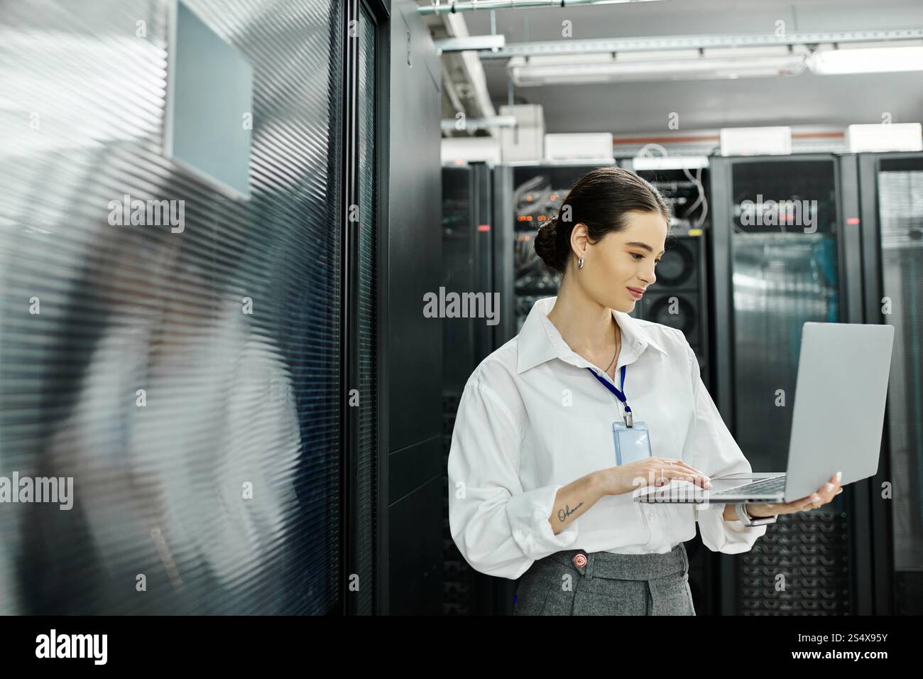 Una donna dedicata con una camicia bianca lavora diligentemente su un notebook in un elegante ambiente di sala server. Foto Stock