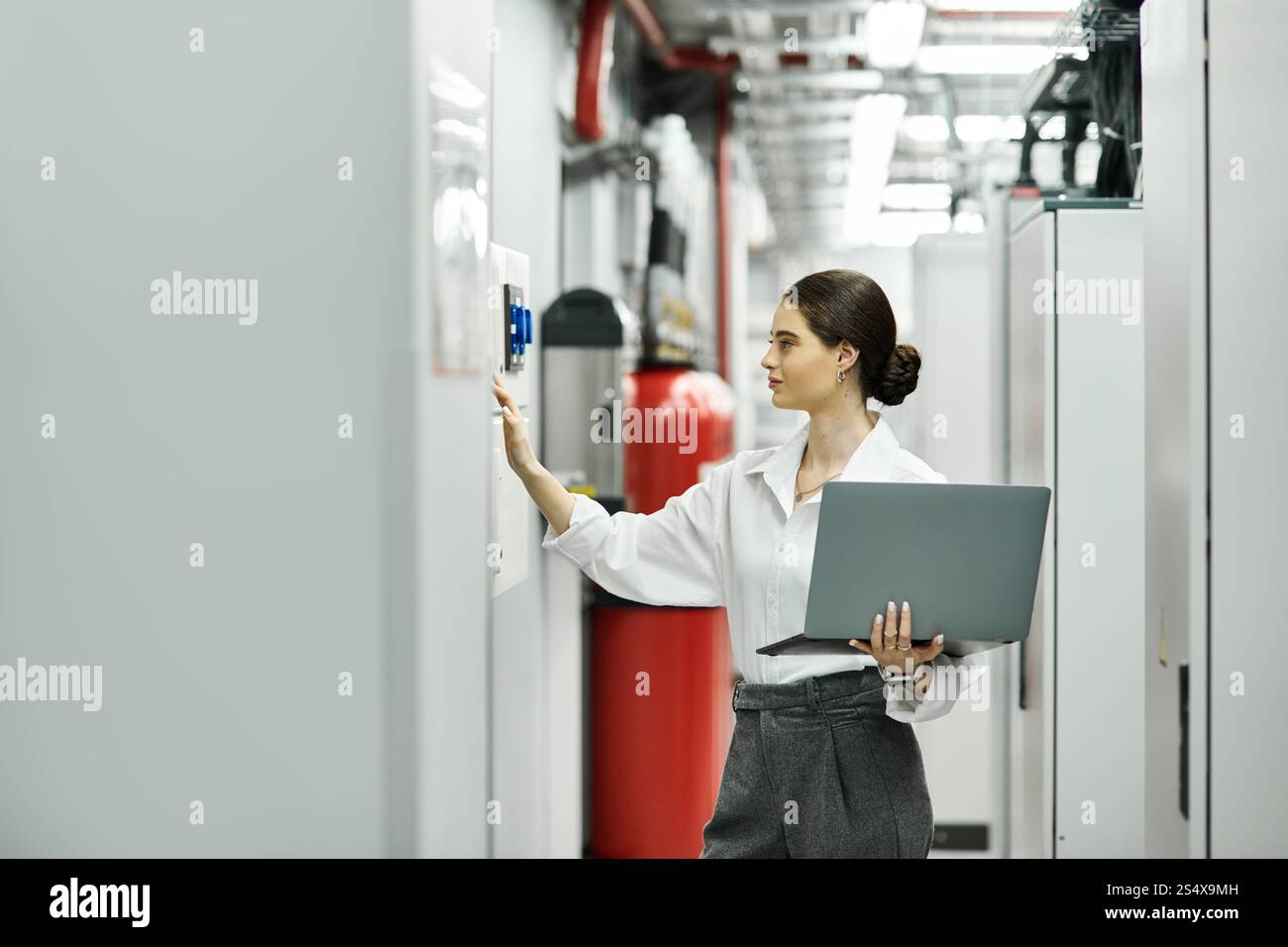 Una donna con una camicia bianca lavora diligentemente, monitorando le apparecchiature in una sala server tecnologicamente esperta. Foto Stock