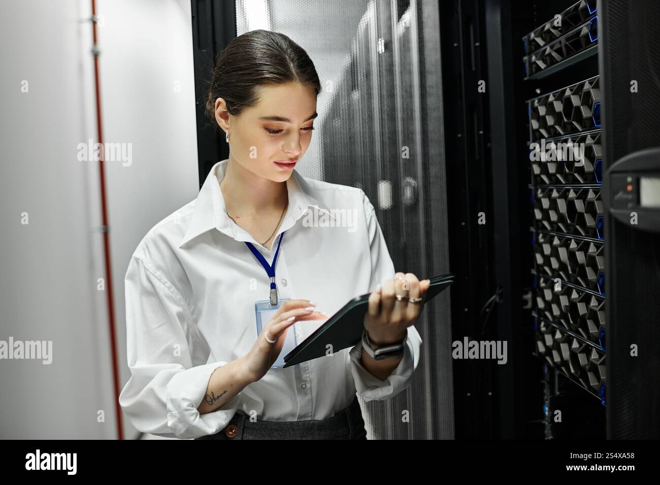 Una donna dedicata con una camicia bianca lavora su un tablet in una vivace sala server. Foto Stock