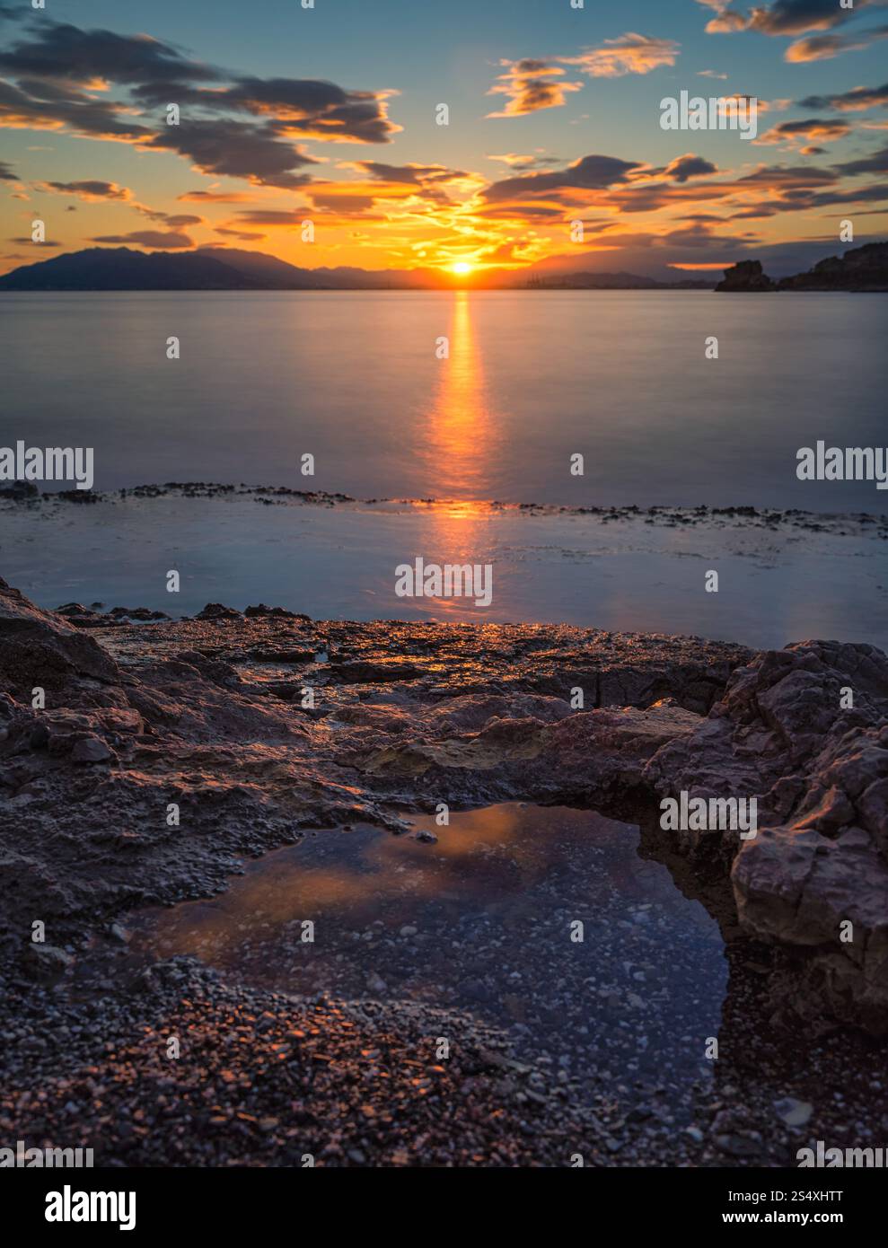 Splendido tramonto su Malaga, con colori vivaci che si riflettono sul mare e piccole pozzanghere tra le formazioni rocciose, creando un'atmosfera tranquilla e panoramica Foto Stock