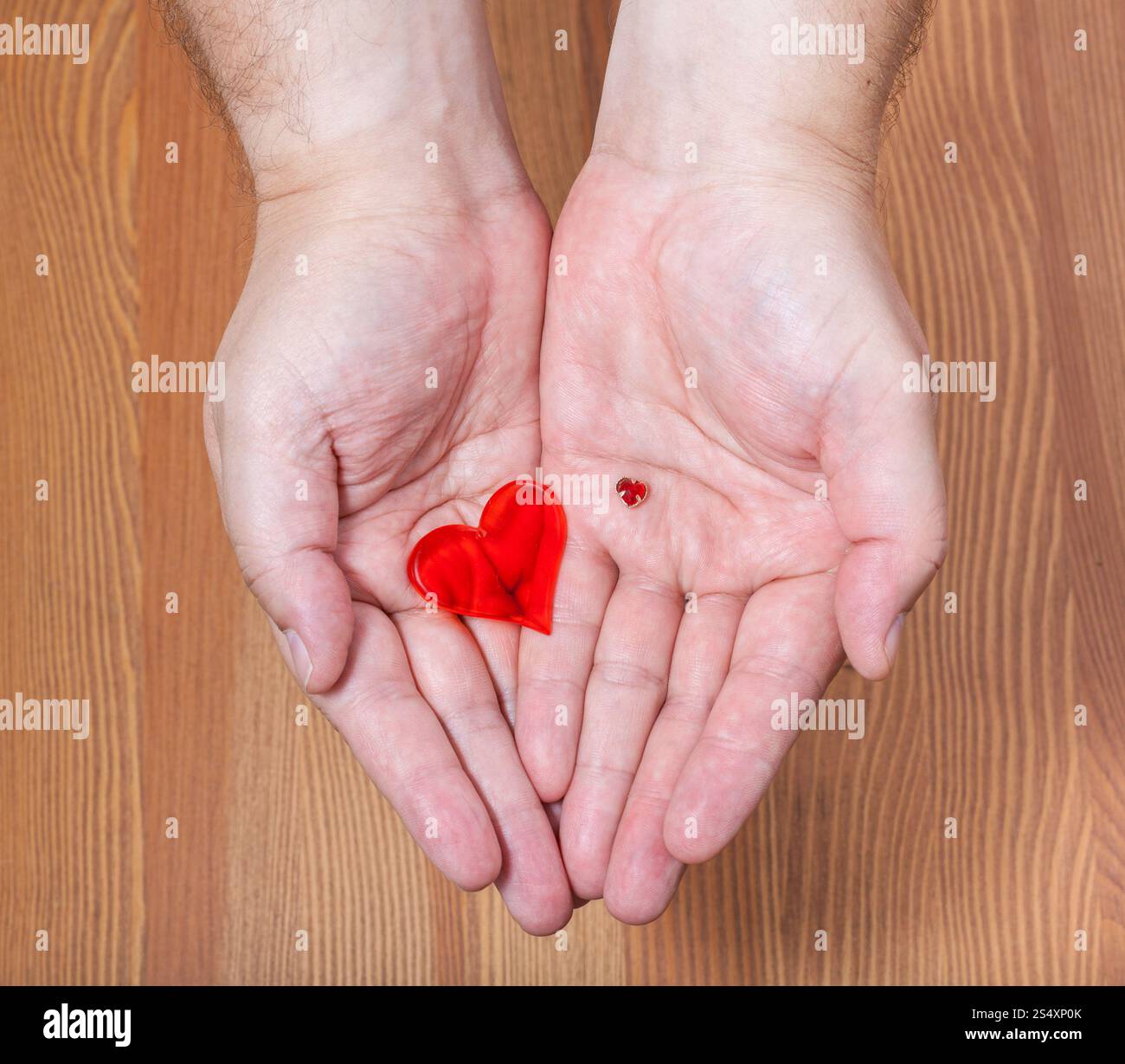 Piccoli e grandi cuori nelle mani di sesso maschile con sfondo di legno Foto Stock