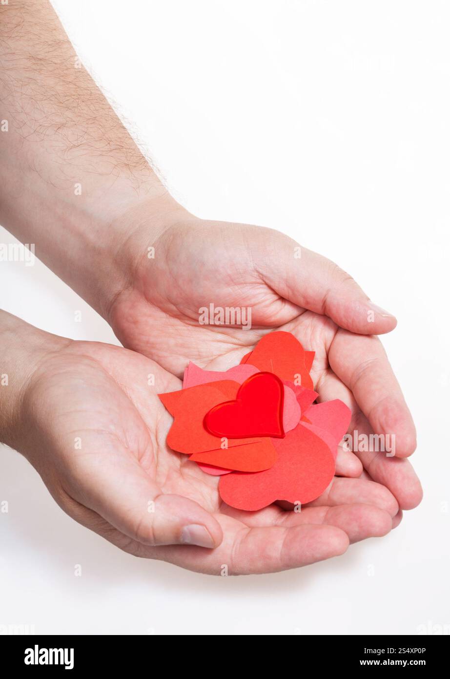 Cuore di vetro sopra la pila di carta cuori sulle palme maschio su sfondo bianco Foto Stock