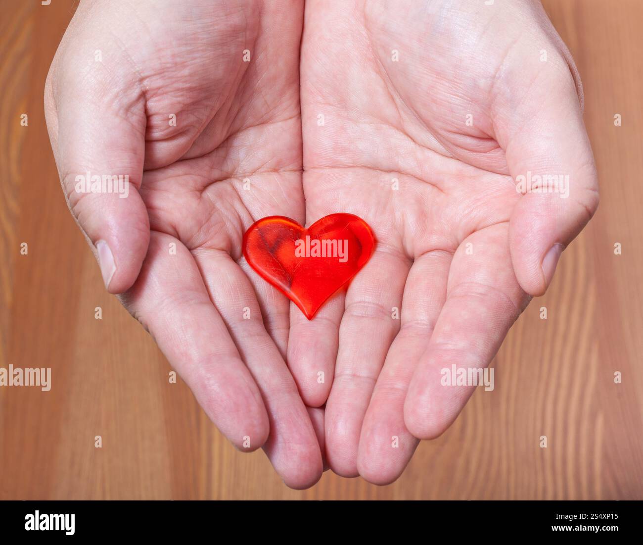 Un cuore rosso sulle palme di sesso maschile con sfondo di legno Foto Stock