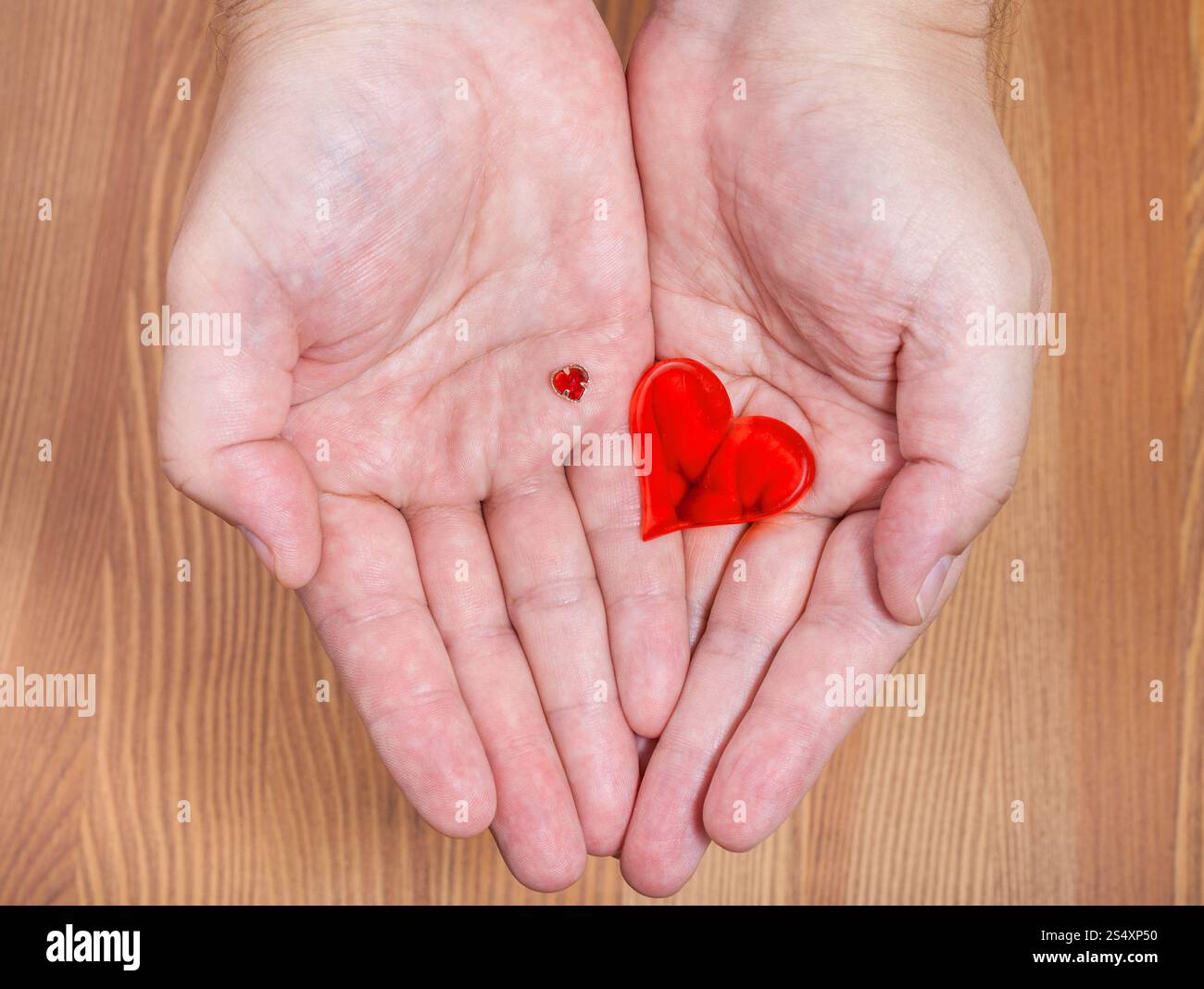 Piccoli e grandi cuori sulle palme di sesso maschile con sfondo di legno Foto Stock